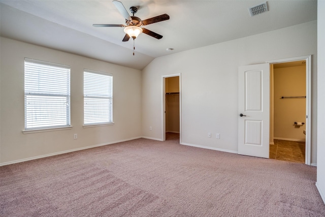 unfurnished bedroom featuring baseboards, carpet flooring, a walk in closet, visible vents, and lofted ceiling