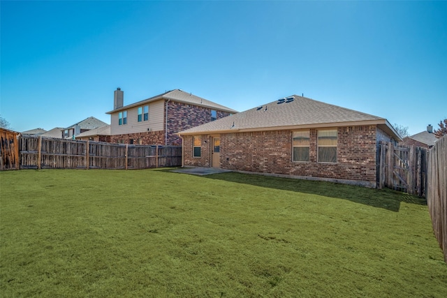 rear view of house with a fenced backyard, roof with shingles, a lawn, and brick siding