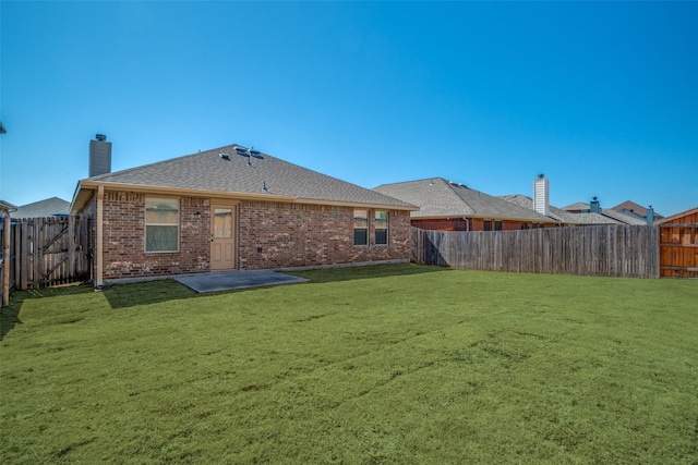 back of property with a fenced backyard, a chimney, a lawn, and brick siding