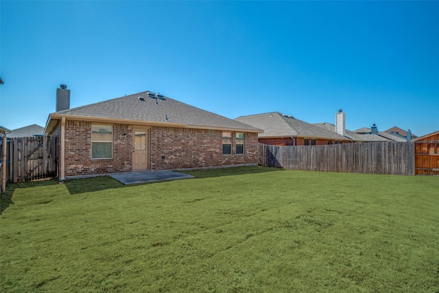 rear view of property featuring brick siding, a yard, a chimney, a fenced backyard, and roof with shingles