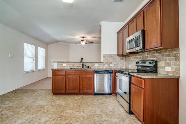 kitchen featuring stainless steel appliances, brown cabinetry, a sink, and a peninsula