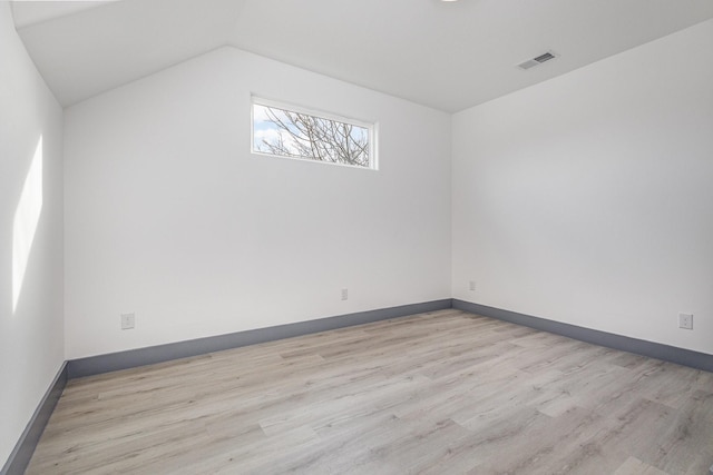 spare room featuring visible vents, light wood-style flooring, baseboards, and lofted ceiling