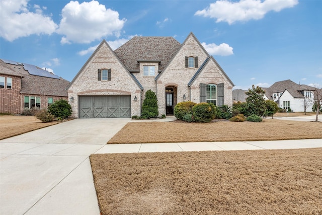 french country home featuring driveway, a front yard, a garage, and brick siding