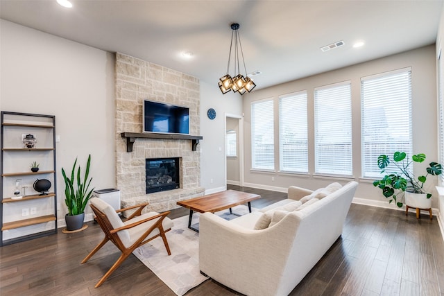 living room featuring a stone fireplace, dark wood-type flooring, visible vents, and baseboards