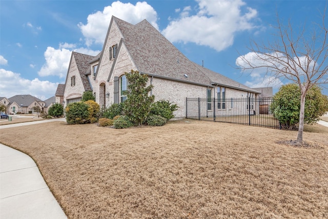 view of side of property featuring a garage, a lawn, roof with shingles, fence, and brick siding