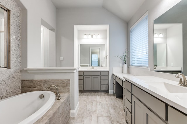 full bath with a bath, two vanities, a sink, and lofted ceiling