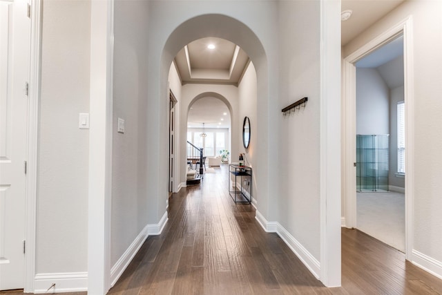 hallway featuring arched walkways, dark wood-style flooring, stairway, and baseboards