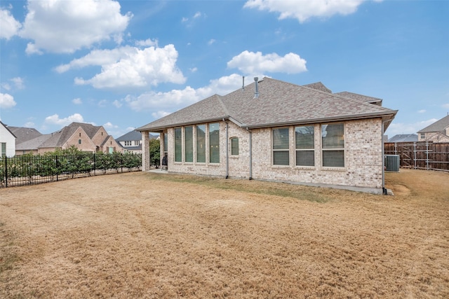 rear view of property with central AC unit, a lawn, a fenced backyard, roof with shingles, and brick siding