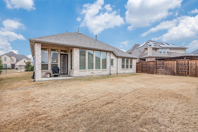 back of house featuring a fenced backyard, brick siding, a yard, roof with shingles, and a patio area