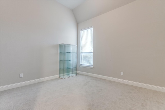 empty room featuring baseboards, vaulted ceiling, and light colored carpet