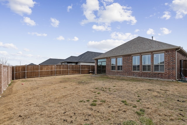 back of property with brick siding, a lawn, a shingled roof, and a fenced backyard