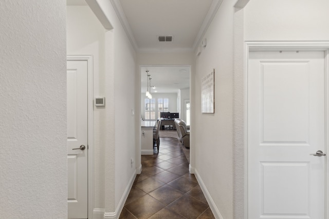 hallway featuring crown molding, visible vents, a textured wall, dark tile patterned floors, and baseboards