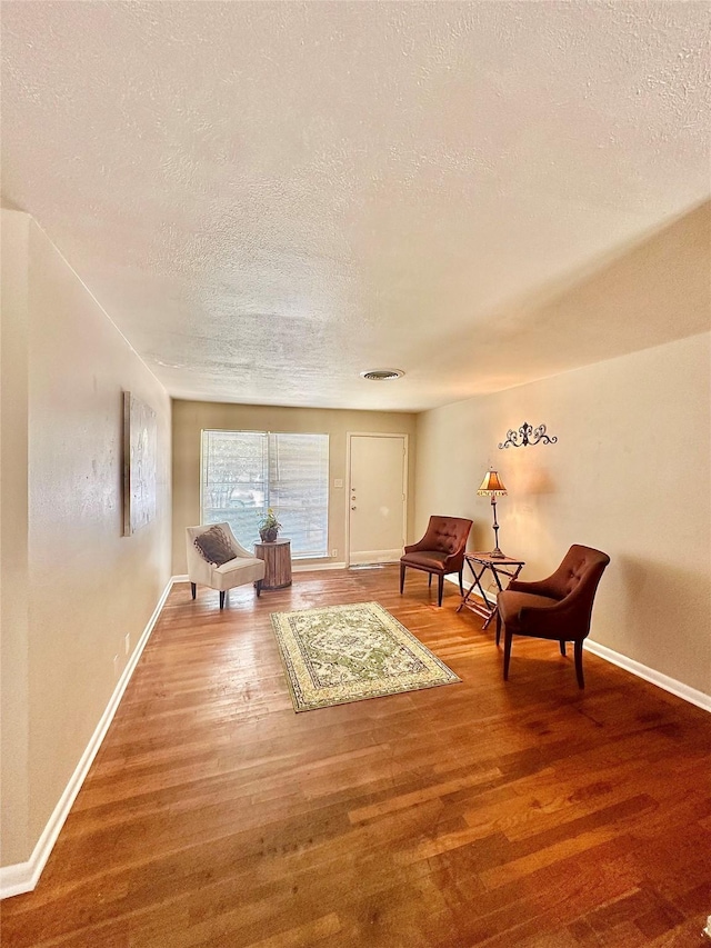 living area with visible vents, a textured ceiling, baseboards, and wood finished floors