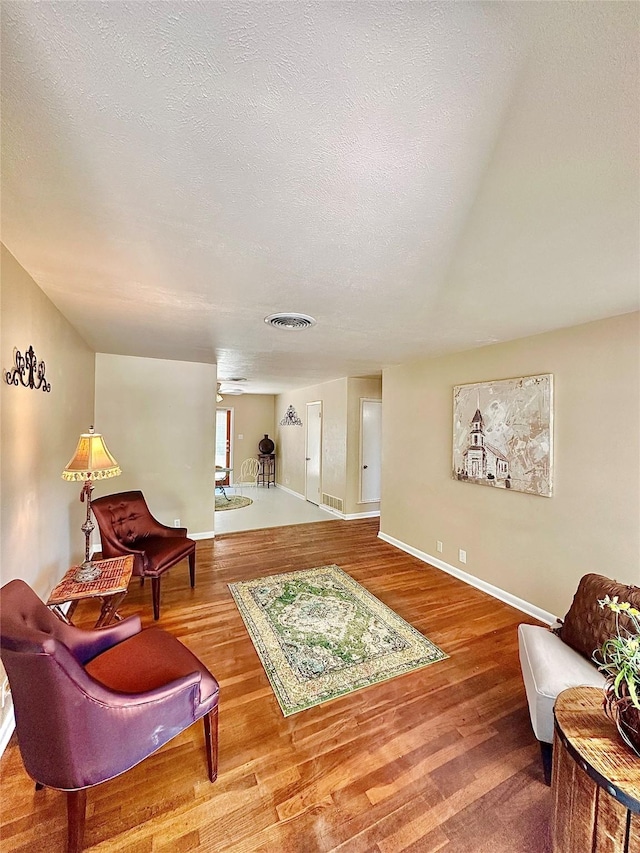 sitting room with visible vents, a textured ceiling, and wood finished floors