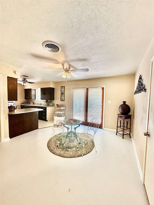 interior space featuring a textured ceiling, visible vents, baseboards, a ceiling fan, and dark brown cabinets