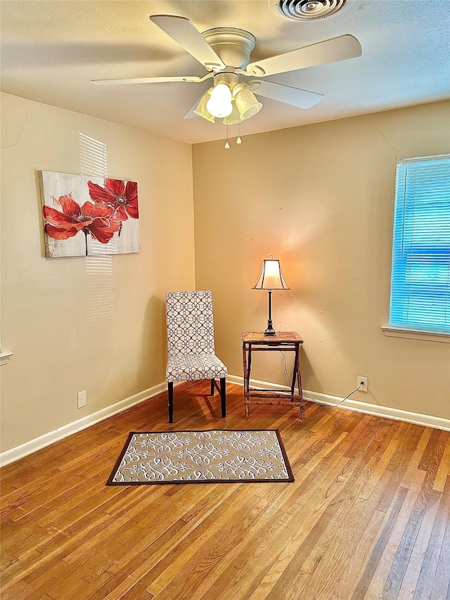 sitting room with a textured ceiling, wood finished floors, visible vents, a ceiling fan, and baseboards