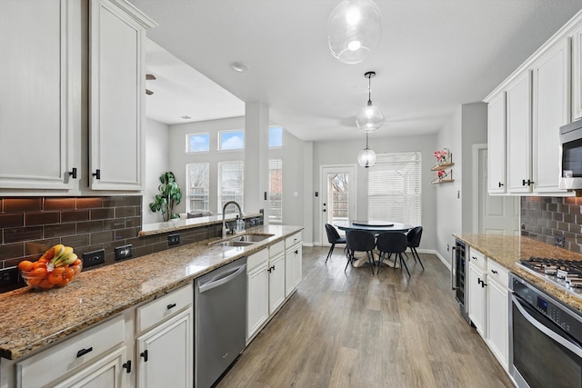 kitchen with light wood-style flooring, appliances with stainless steel finishes, light stone countertops, white cabinetry, and a sink