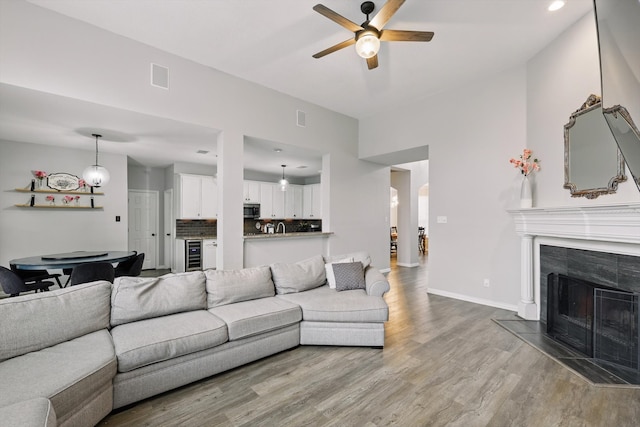 living area with ceiling fan, beverage cooler, wood finished floors, visible vents, and a tiled fireplace