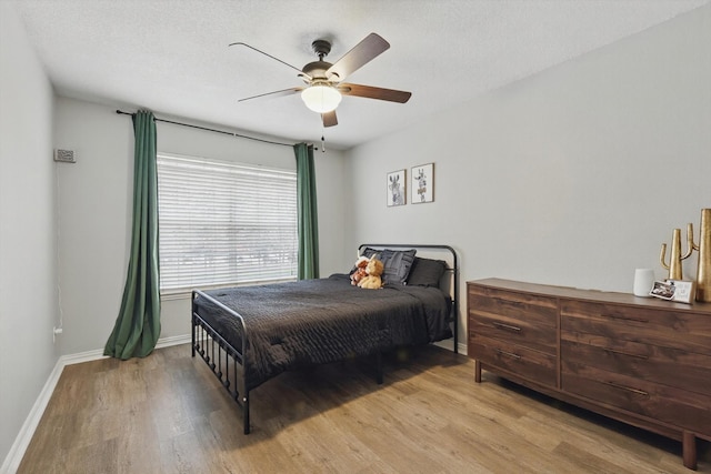 bedroom featuring light wood-type flooring, ceiling fan, baseboards, and a textured ceiling