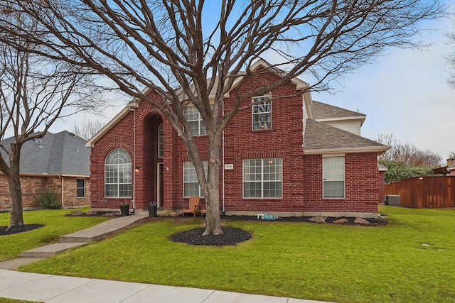 traditional home with brick siding, roof with shingles, a front yard, and fence