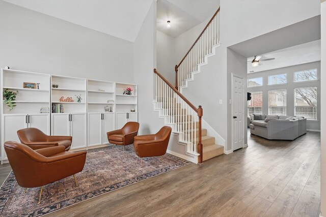 living area featuring a towering ceiling, a ceiling fan, wood finished floors, baseboards, and stairs