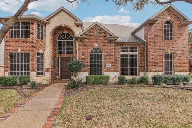 traditional home with a shingled roof, stone siding, brick siding, and a front lawn