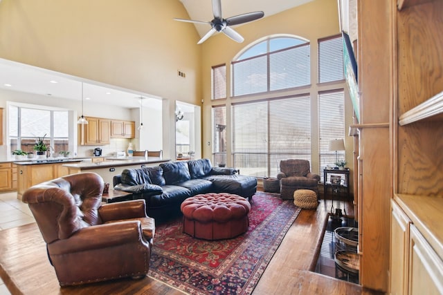 living room featuring a ceiling fan, visible vents, a towering ceiling, and wood finished floors