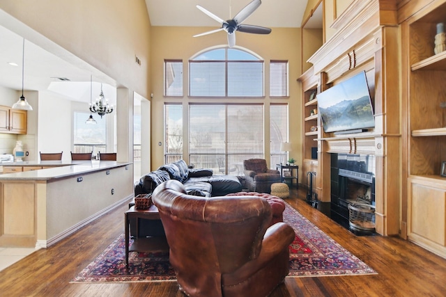 living room featuring dark wood-style flooring, visible vents, a high ceiling, a tile fireplace, and ceiling fan with notable chandelier