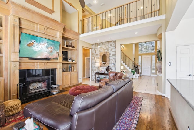 living area featuring built in features, a fireplace, a towering ceiling, and hardwood / wood-style floors