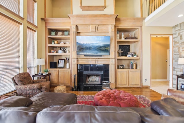 living area with a towering ceiling, a fireplace, built in features, and wood finished floors