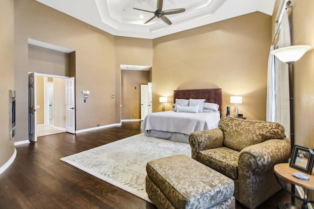 bedroom featuring ceiling fan, a high ceiling, baseboards, dark wood-style floors, and a raised ceiling