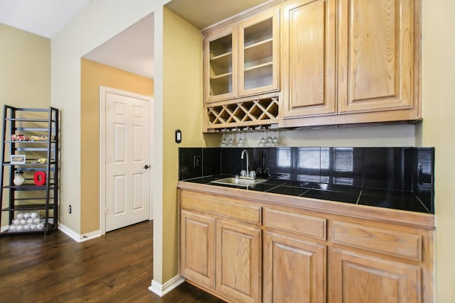 kitchen with dark wood-type flooring, a sink, baseboards, light brown cabinetry, and glass insert cabinets