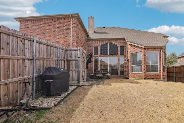 rear view of property featuring roof with shingles, brick siding, a chimney, a lawn, and a fenced backyard