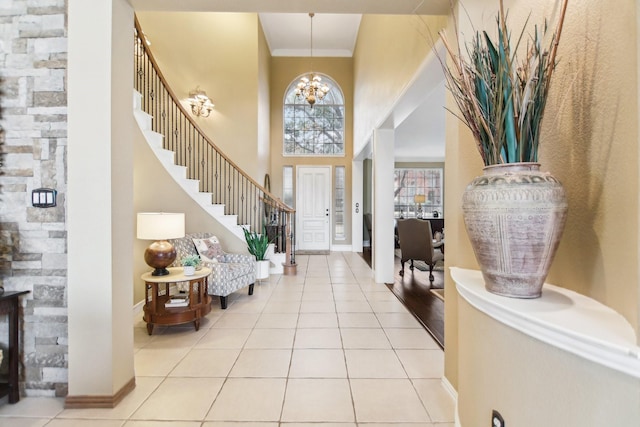 tiled entrance foyer with a towering ceiling, an inviting chandelier, ornamental molding, baseboards, and stairs