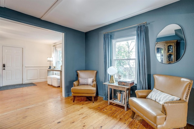 sitting room featuring wood-type flooring, wainscoting, and a decorative wall