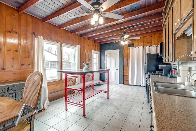 kitchen featuring light tile patterned floors, wood ceiling, a sink, wood walls, and beamed ceiling