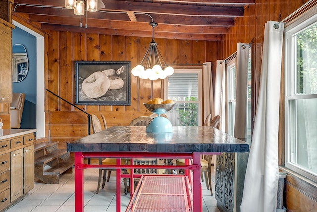 dining area featuring beam ceiling, light tile patterned flooring, plenty of natural light, and wooden walls