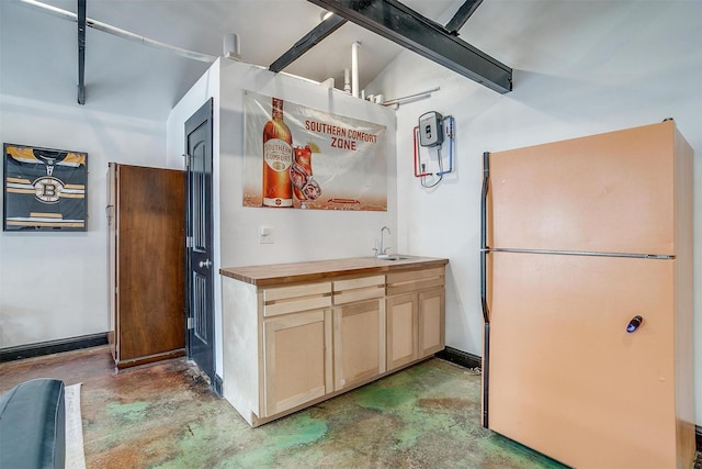 kitchen with concrete flooring, freestanding refrigerator, a sink, and wood counters