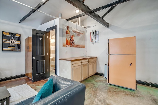 kitchen with baseboards, unfinished concrete flooring, a sink, and freestanding refrigerator