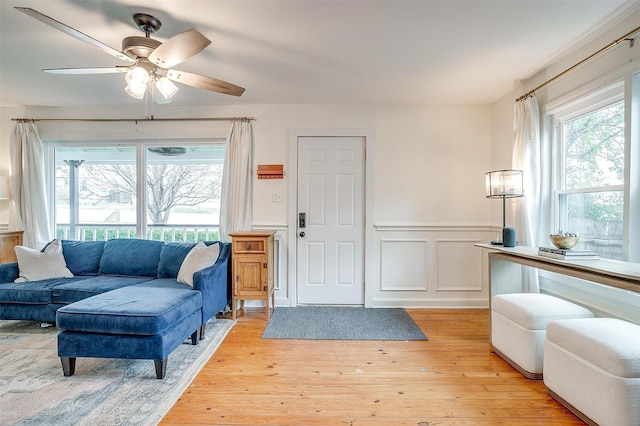 living room featuring a ceiling fan, wainscoting, and light wood-style flooring
