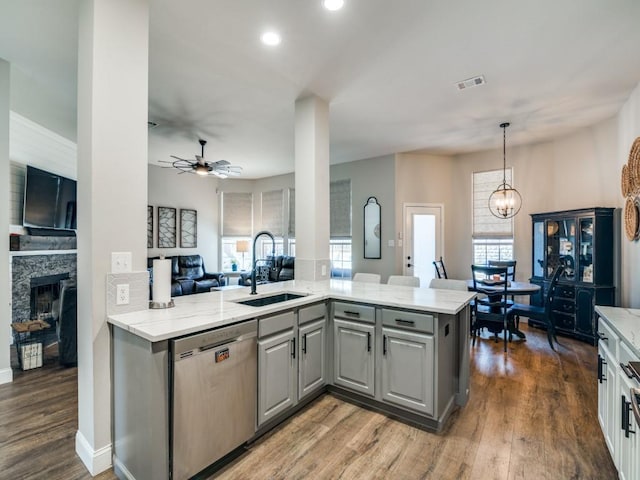 kitchen featuring a stone fireplace, gray cabinetry, a sink, open floor plan, and dishwasher