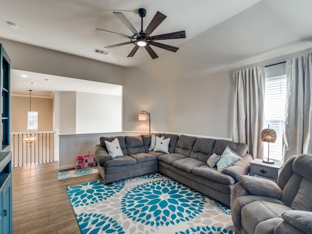 living area featuring visible vents, wainscoting, vaulted ceiling, wood finished floors, and ceiling fan with notable chandelier