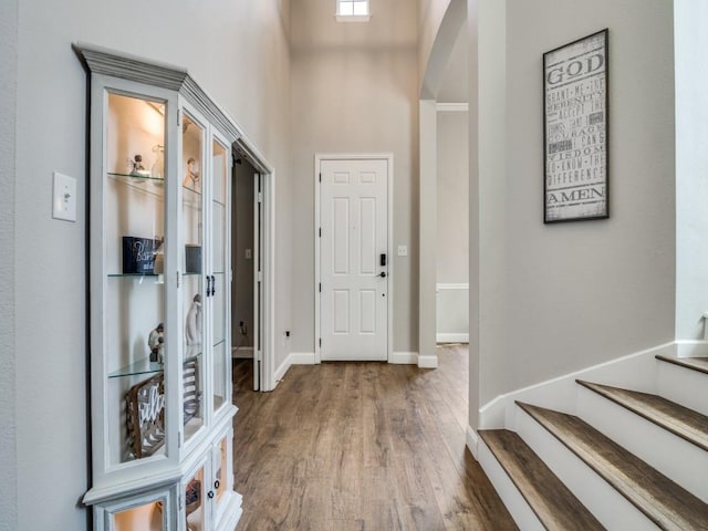 foyer entrance featuring baseboards, arched walkways, a towering ceiling, stairway, and wood finished floors