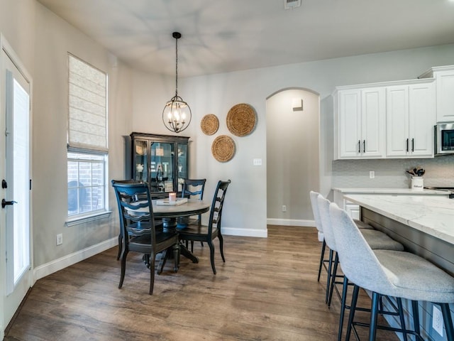 dining room featuring arched walkways, dark wood-type flooring, a notable chandelier, and baseboards