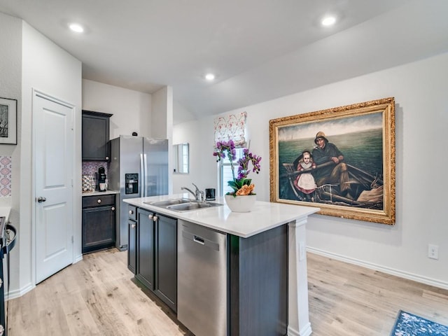 kitchen with stainless steel appliances, light countertops, light wood-style flooring, a kitchen island with sink, and a sink