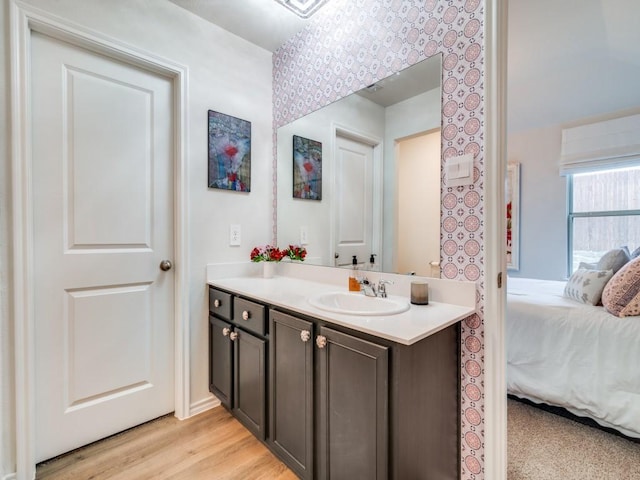 ensuite bathroom with wallpapered walls, connected bathroom, vanity, and wood finished floors