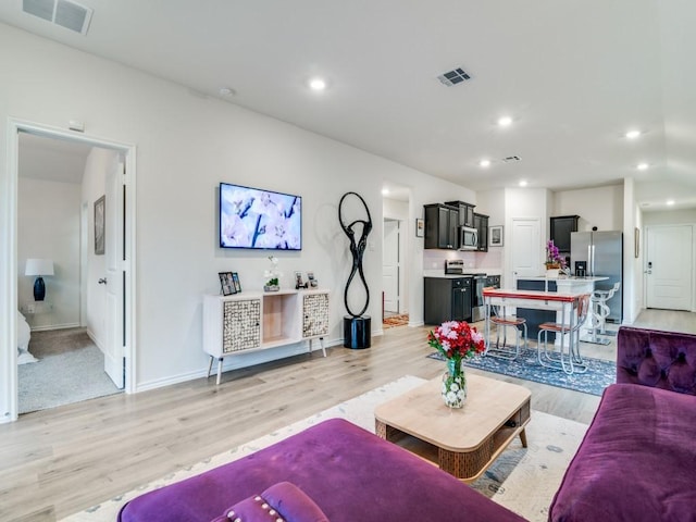 living area featuring baseboards, light wood finished floors, visible vents, and recessed lighting