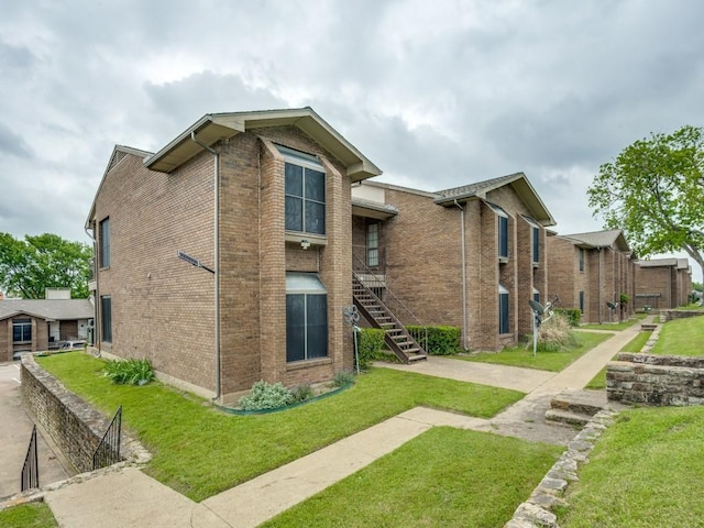 view of side of home with brick siding, a lawn, and stairway