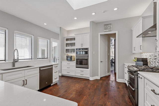 kitchen featuring stainless steel appliances, tasteful backsplash, light countertops, a sink, and wall chimney exhaust hood