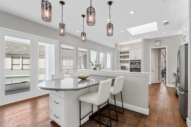 kitchen featuring a skylight, dark wood-style floors, white cabinets, and freestanding refrigerator